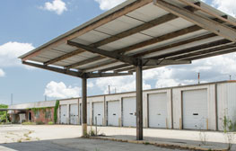 Canopy with nothing under it and white building with several white garage doors