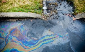 Oil spilled on asphalt with a concrete lip between the asphalt and the grass