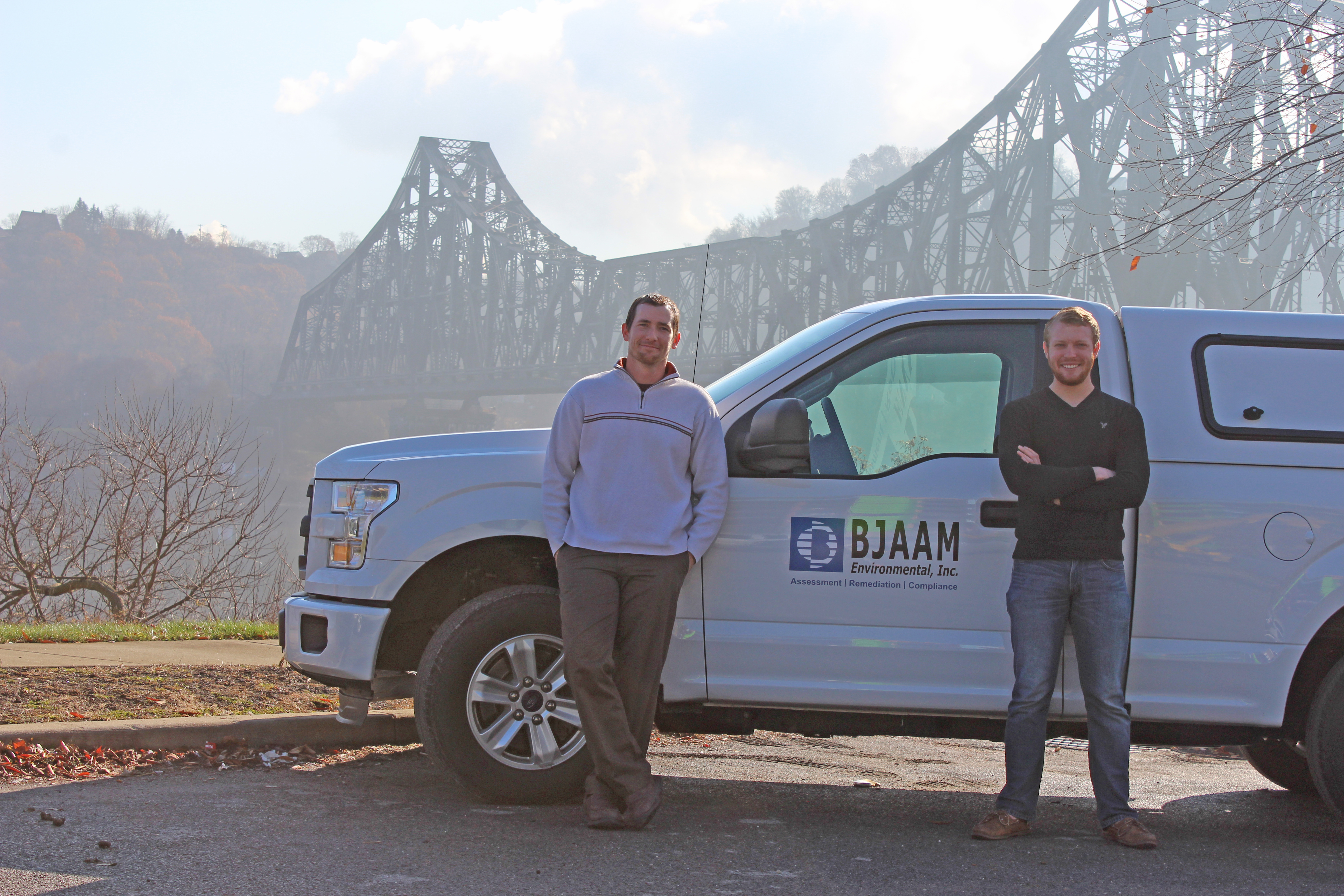 Darren Waddell and Dustin Barnes standing in front of a white truck with BJAAM logo on the door with a bridge in the background